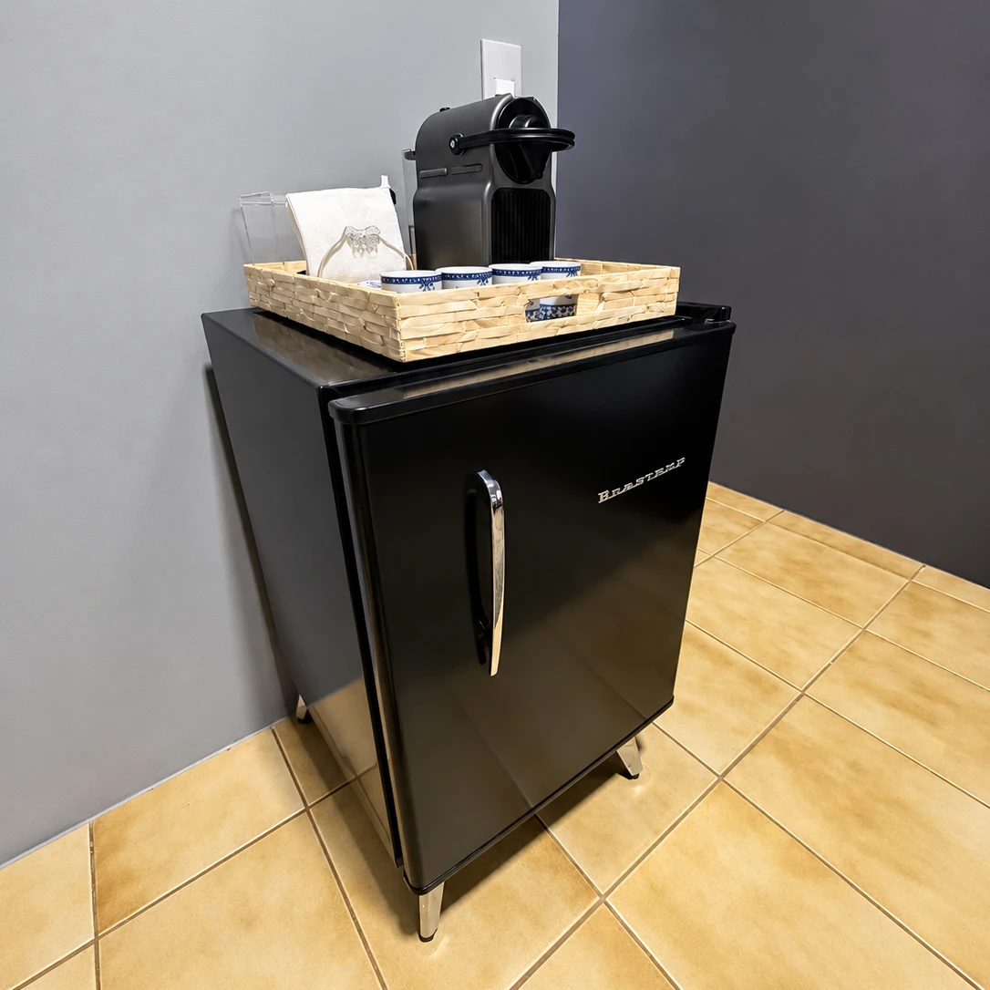 Espaço de apoio com máquina de café, xícaras e frigobar